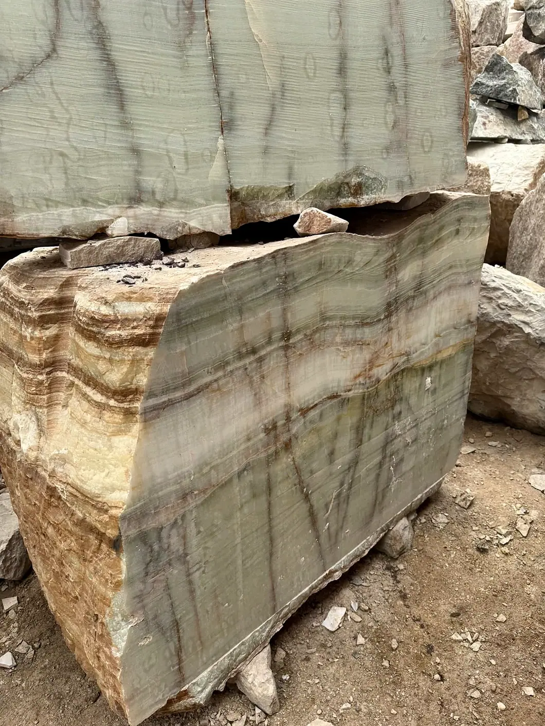 Close-up of a real cut stone block, displaying cream, green and earthy layered veining at the family manufacturing facility